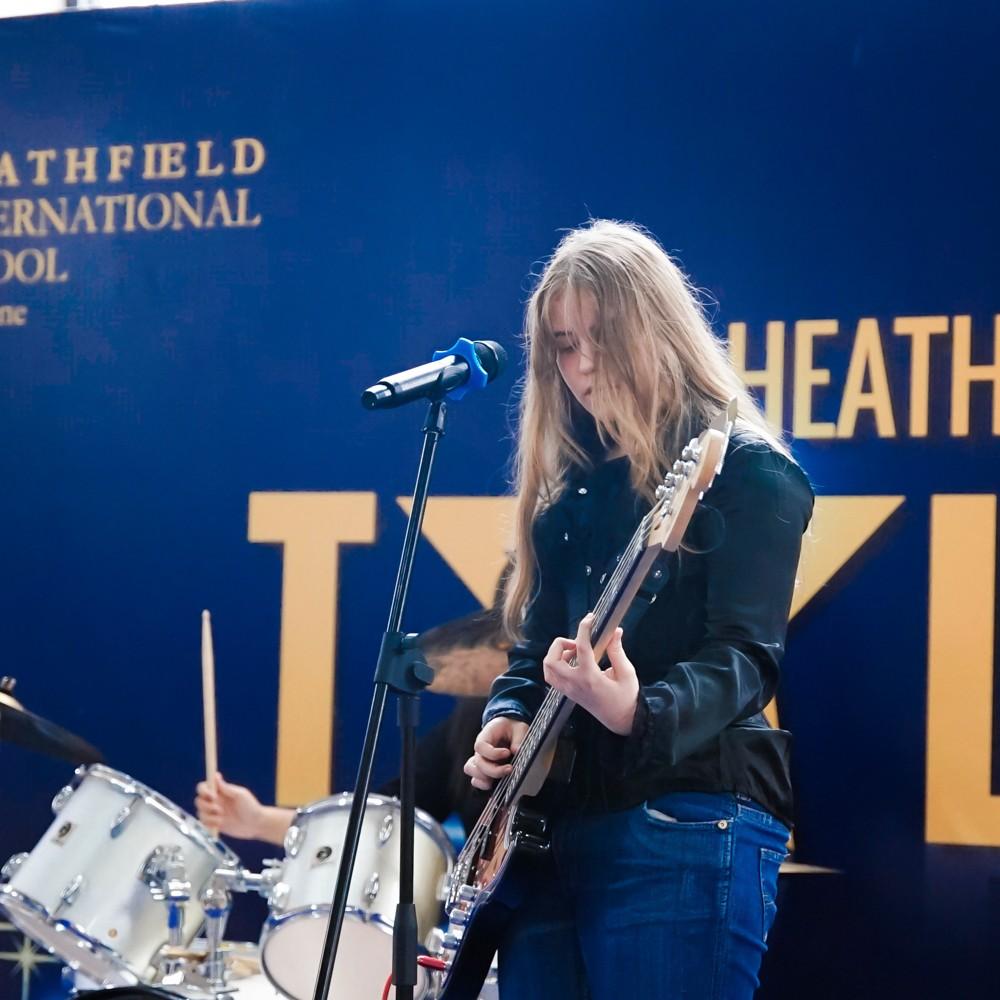Girl plays bass guitar on stage as part of a band performance.