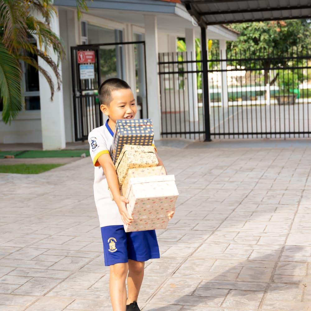 A young student walking with a stack of neatly wrapped gift boxes for the event.