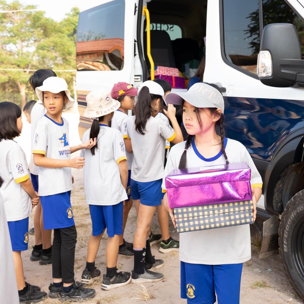 A group of children gathered near the school van, holding and organizing gift boxes for donation.