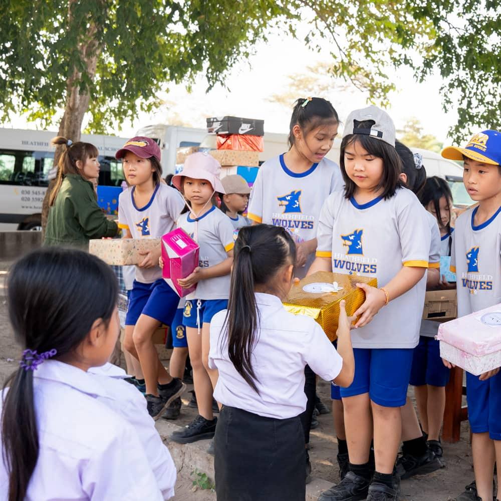 A group of students presenting colorful gift boxes to children from another school as part of the Holiday Box Project.