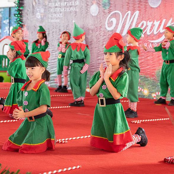 A group of children dressed as festive elves kneels in formation on stage, performing a delightful Christmas-themed routine.