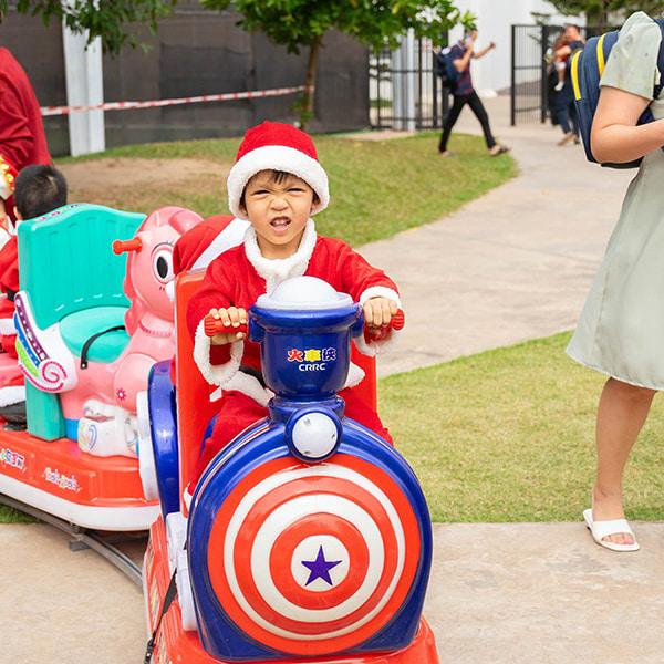 A young child dressed as Santa Claus enjoys a fun ride on a Captain America-themed train at the school event.