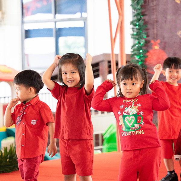 A group of students dressed in red, with one wearing a Christmas-themed sweater, enthusiastically participate in a coordinated performance.