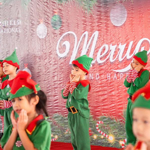 Children dressed as cheerful Christmas elves perform an adorable and festive dance routine on stage.