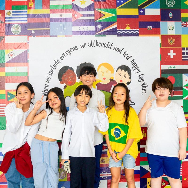 Students posing in front of an international flags backdrop, with some wearing Brazil shirts and others in casual white tops.
