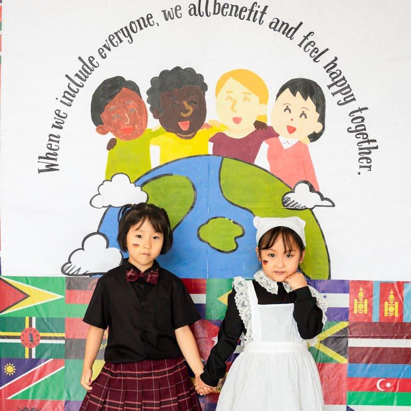 Two students dressed in traditional German-style clothing, standing in front of a mural promoting inclusion and diversity.
