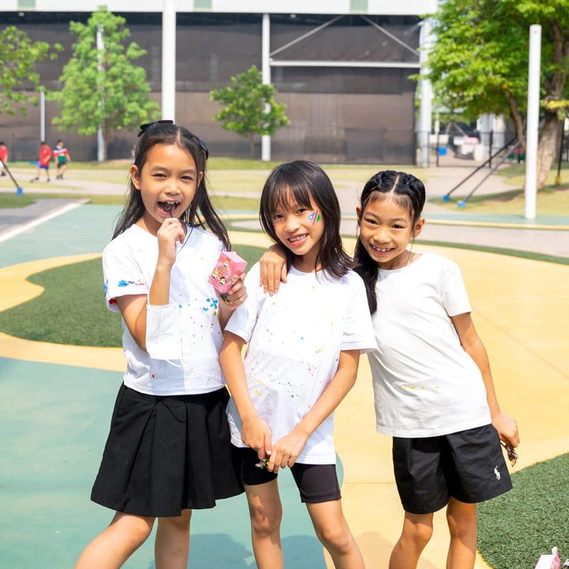 Three girls smiling and posing together outdoors in casual white and black clothing during International Day.