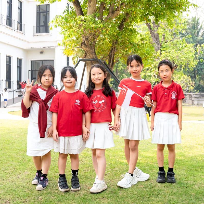 Five girls dressed in red and white posing outside together, representing different countries in matching color themes.