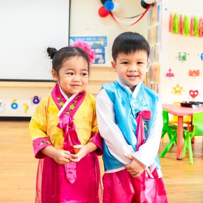 Two children wearing traditional Korean hanbok, smiling in a classroom.