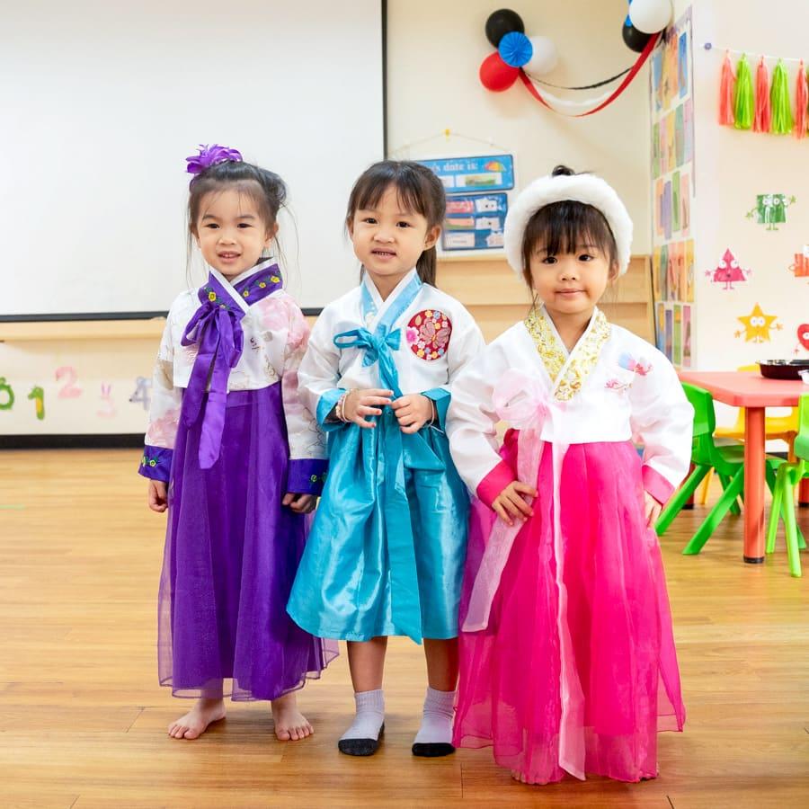 Three girls dressed in vibrant hanbok standing together during International Day.
