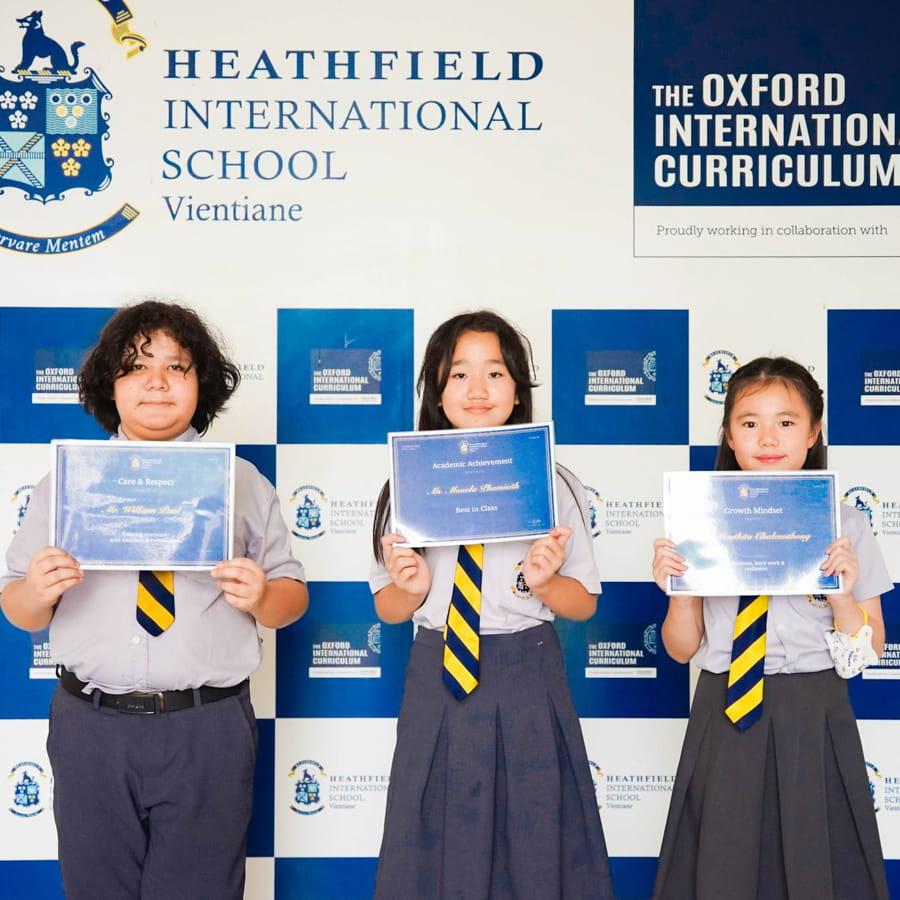Three students smiling and holding achievement certificates