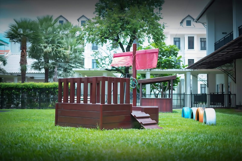An Early Years Foundation Stage (EYFS) playground with a lush green lawn and colorful play equipment.