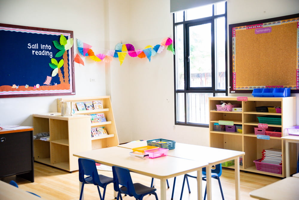 A bright and colorful primary classroom with decorated walls and neatly arranged tables and chairs.
