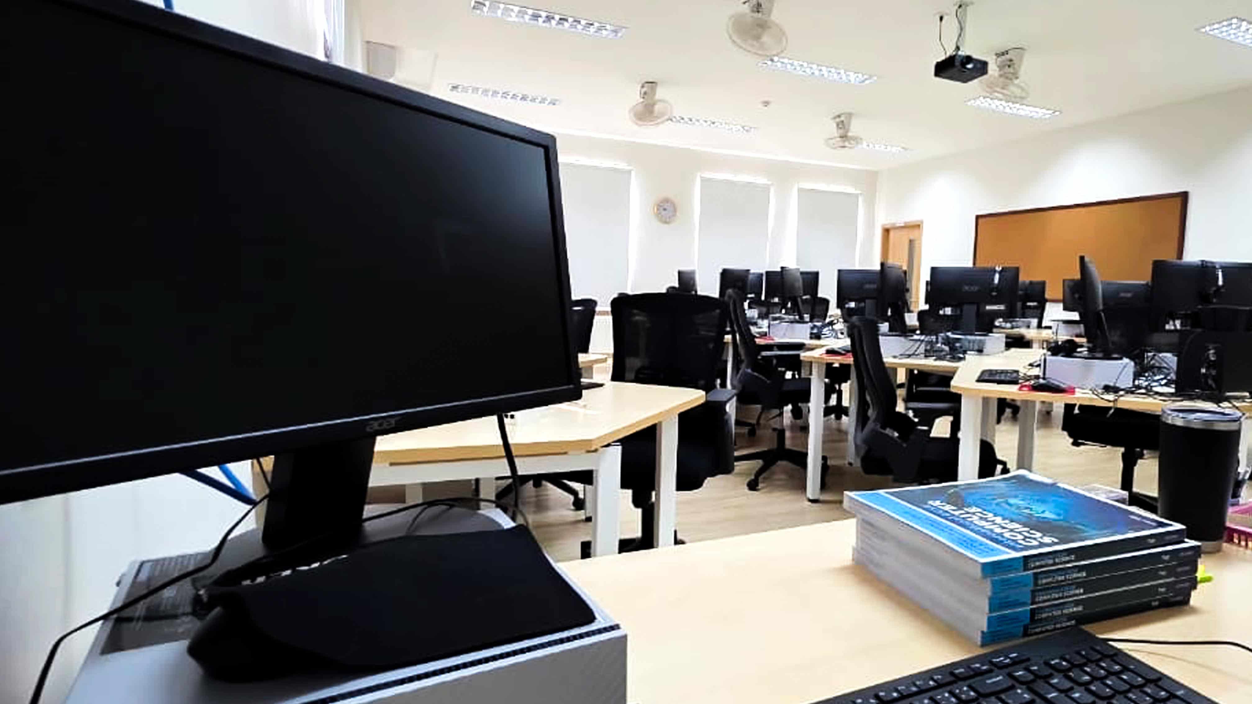 A modern computer lab with rows of desktop computers, ergonomic chairs, and a projector screen at the front, providing a collaborative and tech-enhanced learning environment.
