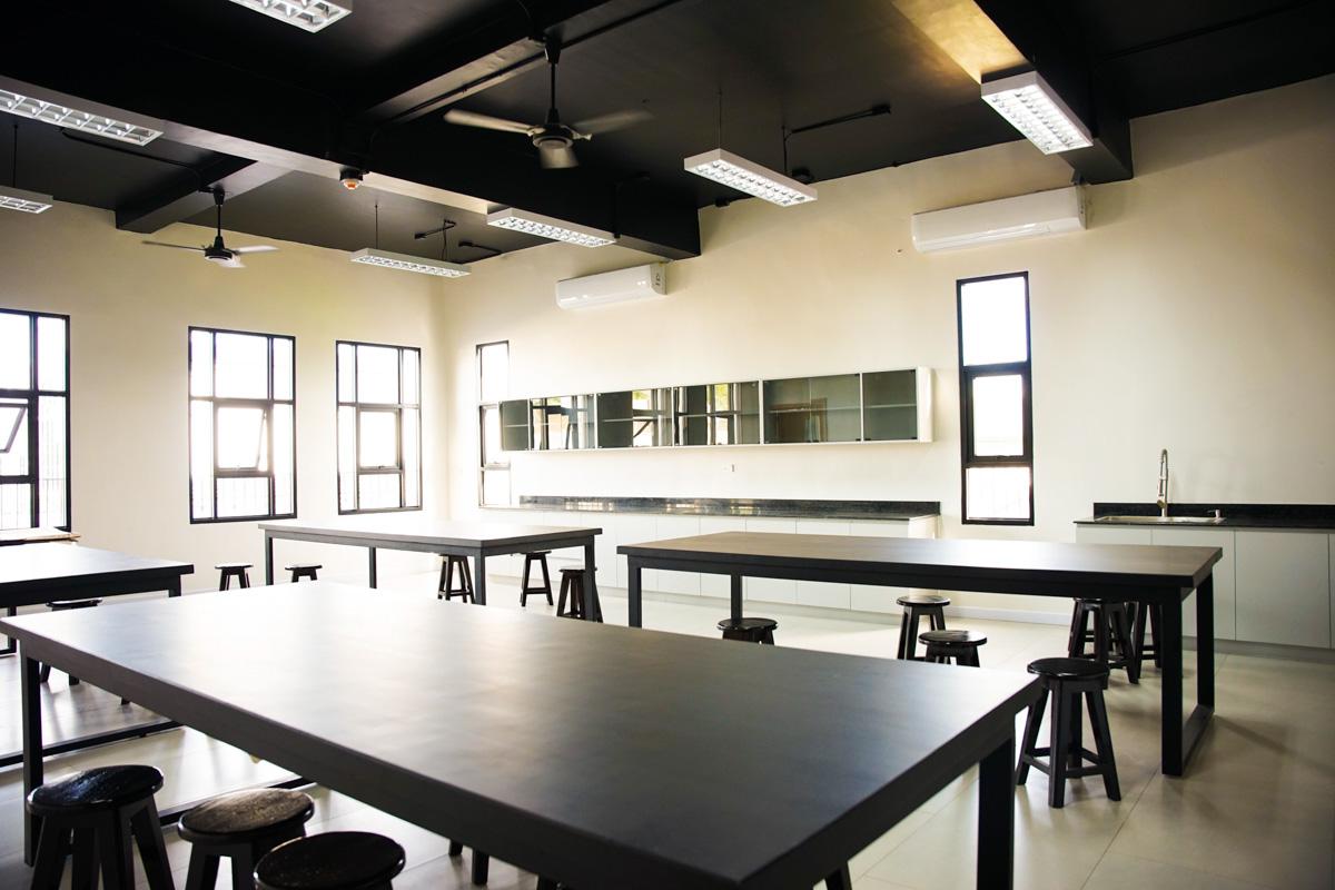 A spacious physics laboratory featuring long black-topped tables and stools, designed for hands-on experiments and learning.