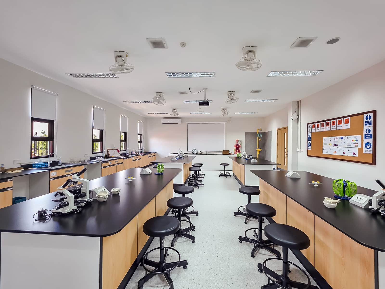 A well-equipped science laboratory with rows of black-topped lab benches, microscopes, and modern teaching equipment.